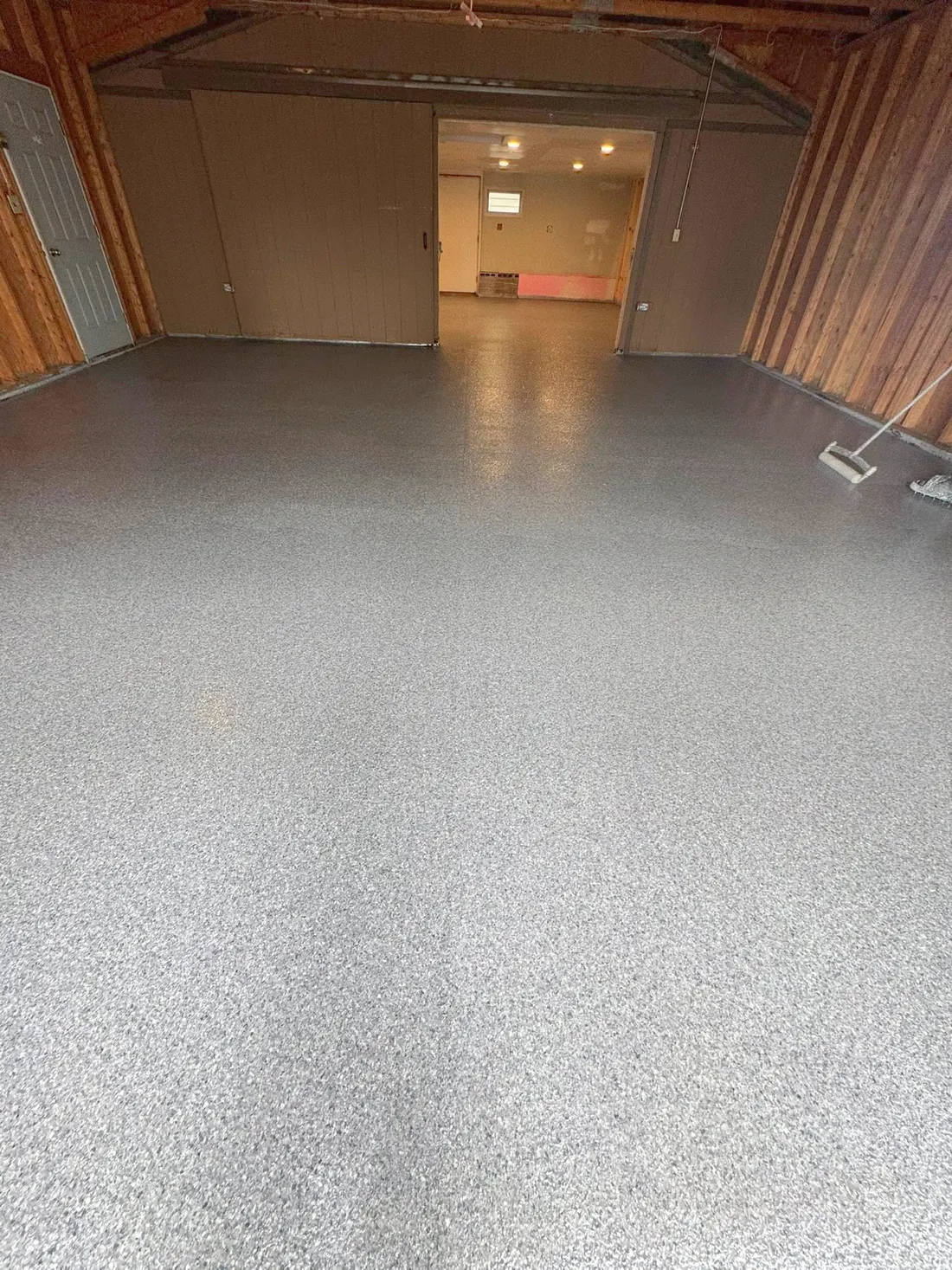 After: the same wood-walled garage with its gray flake-coated floor and finished adjoining room.